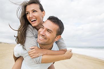 Couple smiling on a beach after being treated for periodontal disease, Garran ACT